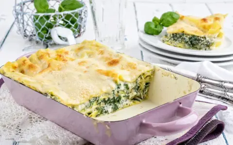 Herzhaftes Spinat-Lasagne-Rezept in einer lila Auflaufform, mit frischem Basilikum garniert.