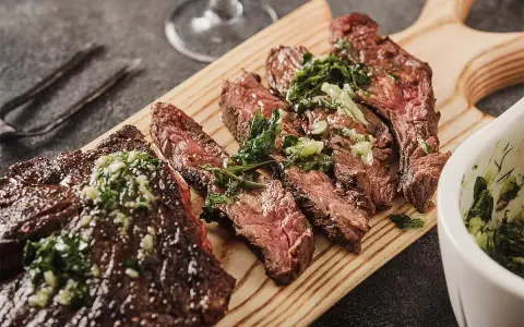 Saftiges, in Scheiben geschnittenes Flank Steak mit Kräutern und einer grünen Sauce auf einem Holzbrett serviert.