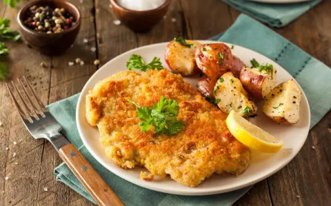 Goldbraunes Schnitzel, perfekt paniert, mit Rosmarinkartoffeln und Zitrone auf einem Teller. Ein Genuss, der zeigt, wie man ein Schnitzel paniert.