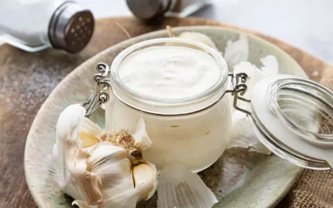 Frische Knoblauchsauce selber machen: cremige Sauce im Glas mit Knoblauchzehen und Salzstreuer im Hintergrund.