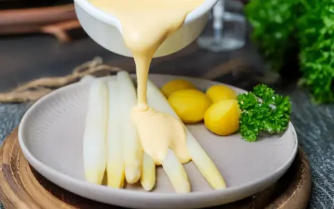 Sauce Hollandaise wird über weißen Spargel und Kartoffeln gegossen, um das Gericht zu verfeinern.