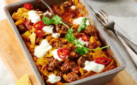 Herzhafter Shepherd's Pie mit Hackfleisch, Tortilla-Chips, Chili-Ringen und Klecksen saurer Sahne, garniert mit Koriander.