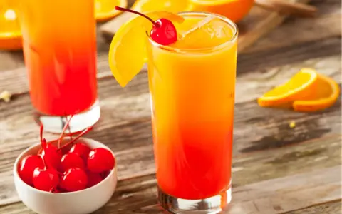 Ein erfrischender Tequila Sunrise mit Orangenscheibe und Kirsche, daneben eine Schale mit Kirschen.
