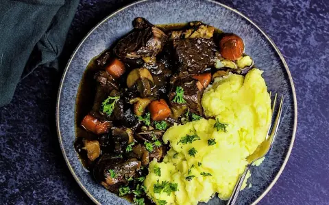 Herzhaftes Boeuf Bourguignon mit zartem Rindfleisch, Karotten und Pilzen, serviert mit cremigem Kartoffelpüree und Petersilie.