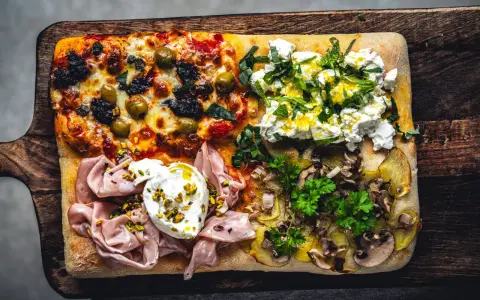 Vier verschiedene Beläge auf einer rechteckigen pizza al taglio: Oliven, Ricotta mit Kräutern, Mortadella mit Burrata und Kartoffeln mit Pilzen.