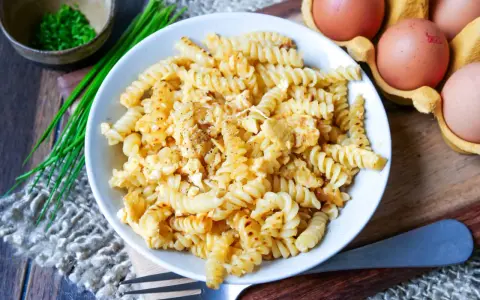 Fusilli-Nudeln mit Rührei, gewürzt mit Pfeffer. Daneben liegen frische Eier und Schnittlauch. Ein einfaches, aber leckeres Gericht: Nudeln mit Ei.