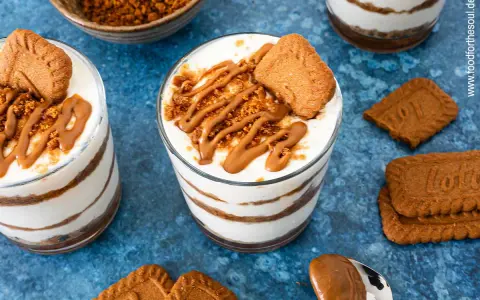 Schichtdessert im Glas: cremiges Lotus Cheesecake mit Keksbröseln und Karamellsoße, garniert mit einem Lotus Keks.