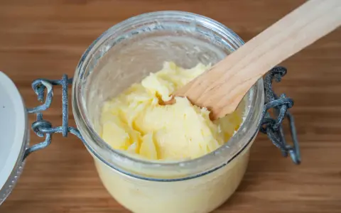 Frisch gemachte Butter in einem Glas, mit einem Holzspatel zum Butter selber machen.
