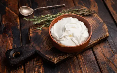 Cremiger, selbstgemachter Haferjoghurt in einer Holzschale, bereit zum Genießen. Ein Löffel und Kräuter liegen daneben.