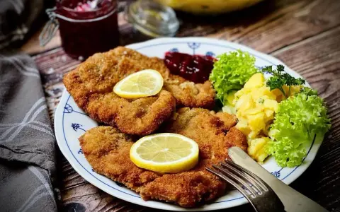 Ein köstlicher **Garnitur Wiener Schnitzel** mit Kartoffelsalat, Preiselbeeren und Zitrone auf einem Teller.