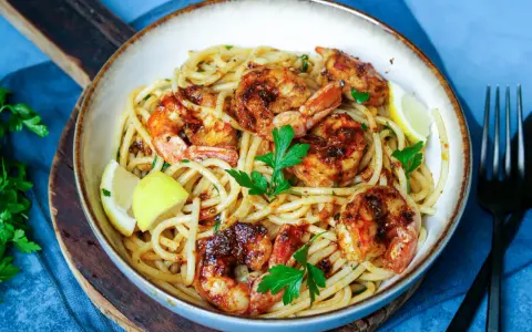 Ein Teller mit köstlichen Spaghetti mit Garnelen, garniert mit frischer Petersilie und Zitronenspalten.