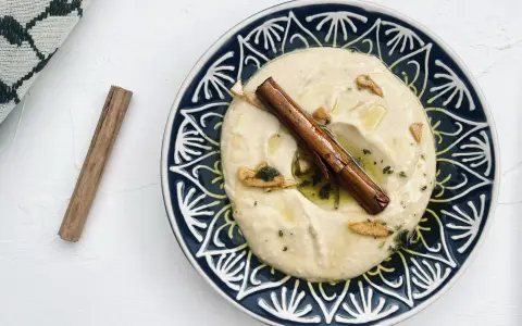 Cremiger Hummus, selbst gemacht, mit Zimtstange und Knoblauch garniert auf einem blau-weißen Teller.