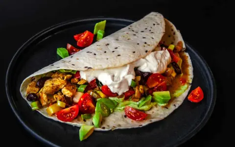 Saftige Fajitas de pollo mit Hähnchen, Gemüse, Avocado und einem Klecks Sauerrahm auf einem Tortilla-Wrap.