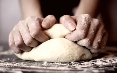 Hände kneten den pizzateig. Wie lange kneten? Bis er geschmeidig ist!