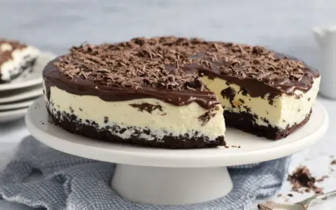 Eine köstliche Bananensplit Torte ohne Backen, mit Schokoladenüberzug und Schokostreuseln. Ein Stück ist bereits angeschnitten.