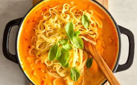 Cremiges Chicken Alfredo mit Tagliatelle, garniert mit frischem Basilikum, in einer schwarzen Pfanne.