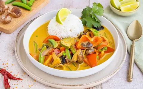 Ein bunter Thai Curry ohne Kokosmilch mit Reis, Paprika, Zucchini und Pilzen, garniert mit Limette und Koriander.