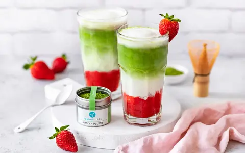Zwei geschichtete Erdbeer-Matcha-Latte-Getränke mit frischen Erdbeeren und Matcha-Pulver.
