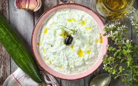 Frischer Tzatziki selbst machen: Cremiger Joghurt mit Gurke, Knoblauch, Dill und Olivenöl. Dazu eine Olive und Kräuter.