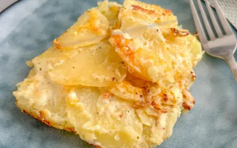 Ein Stück Kartoffelgratin einfach mit Sahne, goldbraun gebacken, auf einem blauen Teller. Daneben eine Gabel.
