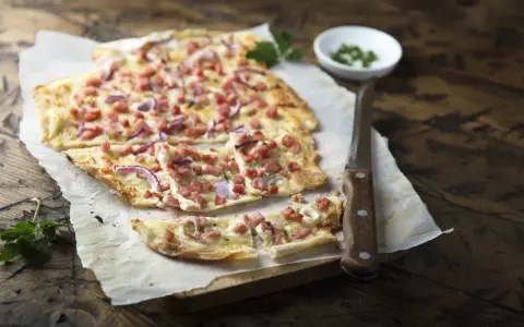 Flammkuchen mit Speck und Zwiebeln, eine klassische Idee für Flammkuchen Belag. Frisch und knusprig auf Holz serviert.