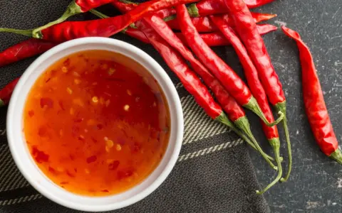 Frische rote Chilis neben einer Schüssel mit selbstgemachter Chili-Sauce. Perfekt zum Chili Sauce selber machen!