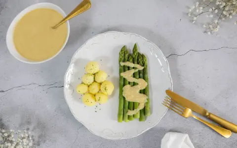 Spargel mit kleinen Kartoffeln und einer cremigen, veganen Sauce Hollandaise. Ein goldener Löffel liegt in der Sauce.