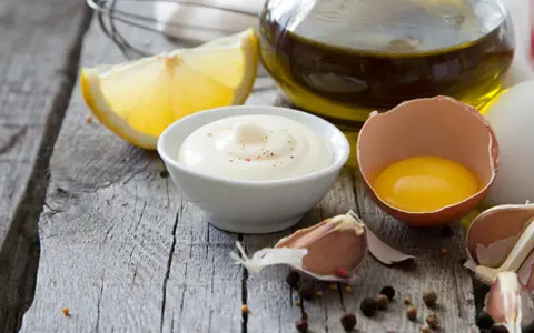 Cremige Mayonnaise mit gekochtem Eigelb und Joghurt, garniert mit Pfeffer, neben Zitrone, Knoblauch und Olivenöl.