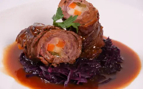 Zwei Rouladen mit Gemüsefüllung, serviert mit Rotkohl und Bratensoße. Köstliche Rouladen im Backofen zubereitet.