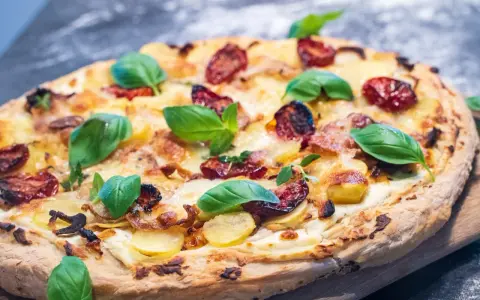 Eine köstliche Pizza Bianca mit Kartoffelscheiben, getrockneten Tomaten und frischem Basilikum.