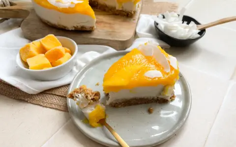 Ein cremiges Mango Cheesecake ohne Backen, garniert mit Kokosflocken. Ein Stück wird gerade mit einem Löffel probiert.