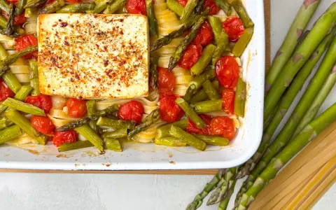 Spargel, Kirschtomaten und Pasta mit einem Block Feta, gewürzt mit Kräutern, in einer Auflaufform.