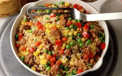 Reis mit Hackfleisch, Erbsen, Mais und Paprika in einer Schüssel, serviert mit einer Gabel.