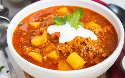 Herzhafte Mitternachtssuppe mit Hackfleisch und Sauerkraut, garniert mit einem Klecks Sauerrahm und Petersilie.