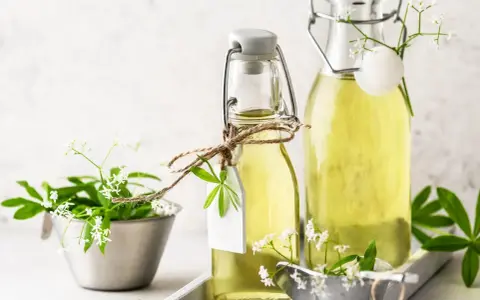 Zwei Flaschen mit selbstgemachtem Waldmeistersirup, dekoriert mit frischem Waldmeister.