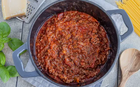 Herzhaftes Bolognese-Rezept original in einem Topf, mit frischem Basilikum, Parmesan und Spaghetti daneben.