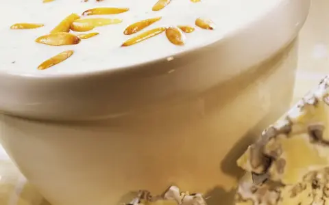 Cremige Gorgonzola-Sauce mit gerösteten Pinienkernen in einer Schüssel, daneben ein Stück Gorgonzola.