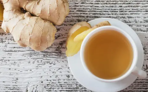 Frischer Ingwer und eine Tasse Ingwertee auf Holzhintergrund. Vielleicht ein kleiner Fehler bei der Zubereitung, wenn der Tee zu stark ist.
