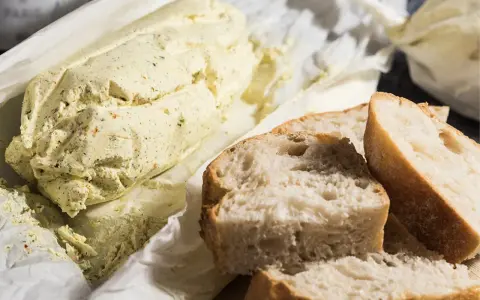 Ein Laib Kräuterbutter, wie Cafe de Paris Butter, liegt neben frisch geschnittenem Baguette.