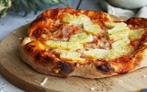 Eine köstliche Pizza Hawaii mit saftigen Ananasstücken und Schinken auf knusprigem Teig, garniert mit Kräutern.
