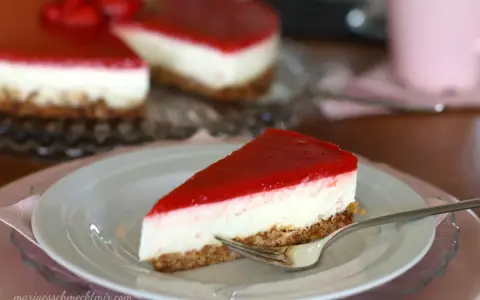Ein Stück New York Cheesecake ohne Backen mit rotem Fruchttopping auf einem Teller, daneben ein ganzer Kuchen.