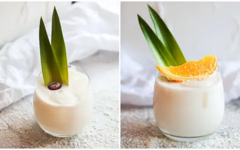 Zwei Gläser cremiger, alkoholfreier Piña Colada, garniert mit Ananasblättern und einer Orangenscheibe bzw. einer Beere.