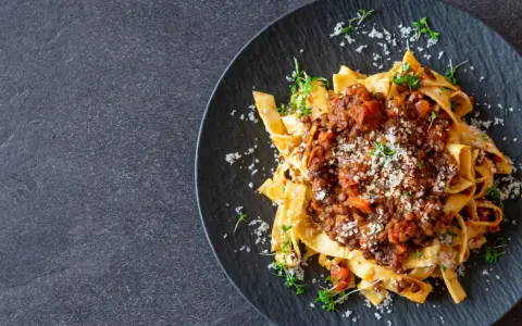 Jamie Oliver Bolognese auf Bandnudeln, garniert mit frischen Kräutern und Parmesan. Ein herzhaftes Gericht, das Lust auf mehr macht.