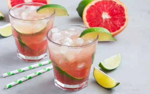 Erfrischender Aperol Paloma mit Grapefruit und Limette, serviert mit Eis und grünen Trinkhalmen.