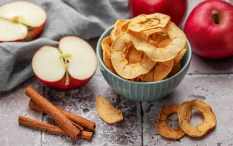 Leckere Apfelchips, die man ganz einfach selber machen kann, in einer Schüssel mit frischen Äpfeln und Zimtstangen.