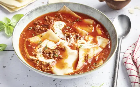 Herzhafte Lasagne Suppe in einer Schüssel, mit Hackfleischsauce, Nudelplatten und einem Klecks Sahne. Frisch garniert mit Basilikum.