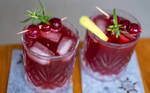 Zwei erfrischende, rote Mocktails mit Kirschen und Rosmarin, perfekt für einen entspannten Abend.