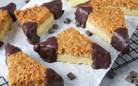 Dreiecke von einem Nussecken Rezept, mit Schokoladenboden und knuspriger Nussdecke, auf Backpapier arrangiert.