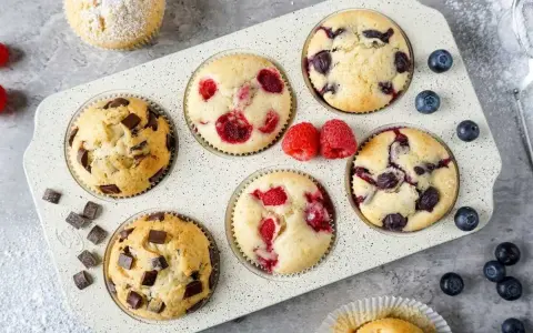 Leckeres Muffins Rezept: Schoko-, Himbeer- und Blaubeermuffins in einer Form, daneben frische Beeren und Schokostückchen.