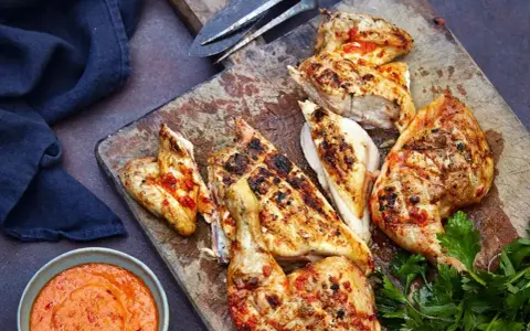 Saftiges Peri Peri Chicken, gegrillt und mit einer würzigen Sauce serviert, liegt auf einem Holzbrett.